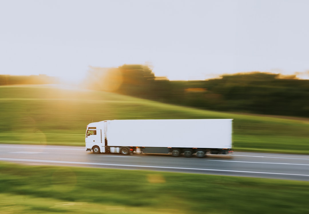 A white semi truck hauling freight along a rural highway